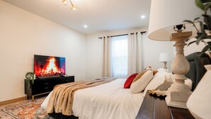 Ett sovrum med en säng, en tv som visar en eld, en lampa och en växt.