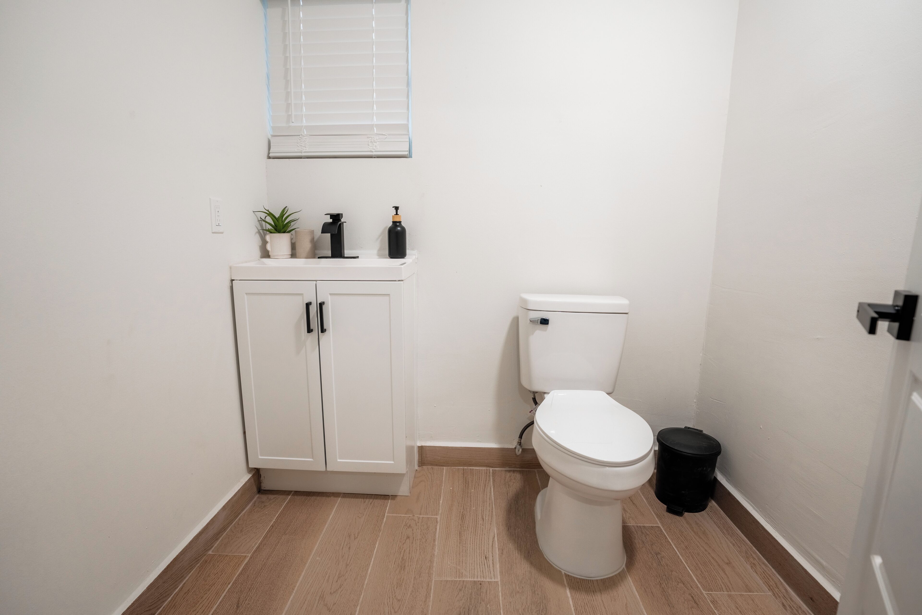 Ein kleines, sauberes Badezimmer mit Toilette, einem Schrank und einem Mülleimer.