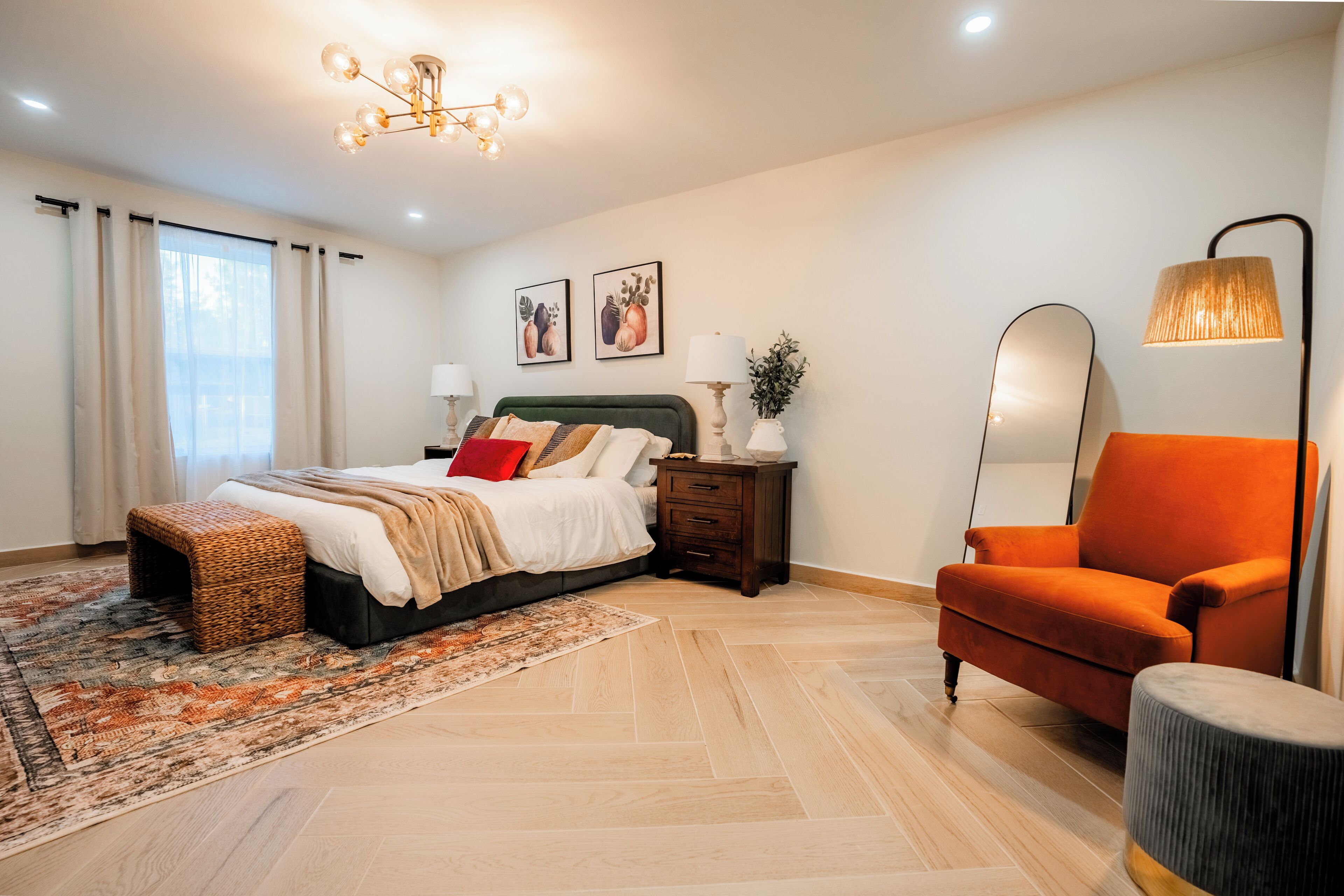 A modern bedroom with a bed, nightstands, a chair, and a large mirror.