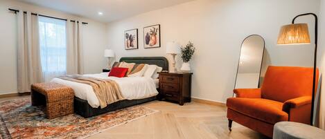 A modern bedroom with a bed, nightstands, a chair, and a large mirror.