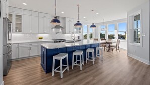 A modern kitchen with white cabinets, a central island with bar stools, and pendant lighting. - Luxury beach home w/oceanviews, 5-BR private pool, elevator, only steps to beach (North Topsail Beach)