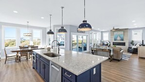 A modern kitchen with a central island, pendant lighting, and a view of the outdoors. - Luxury beach home w/oceanviews, 5-BR private pool, elevator, only steps to beach (North Topsail Beach)