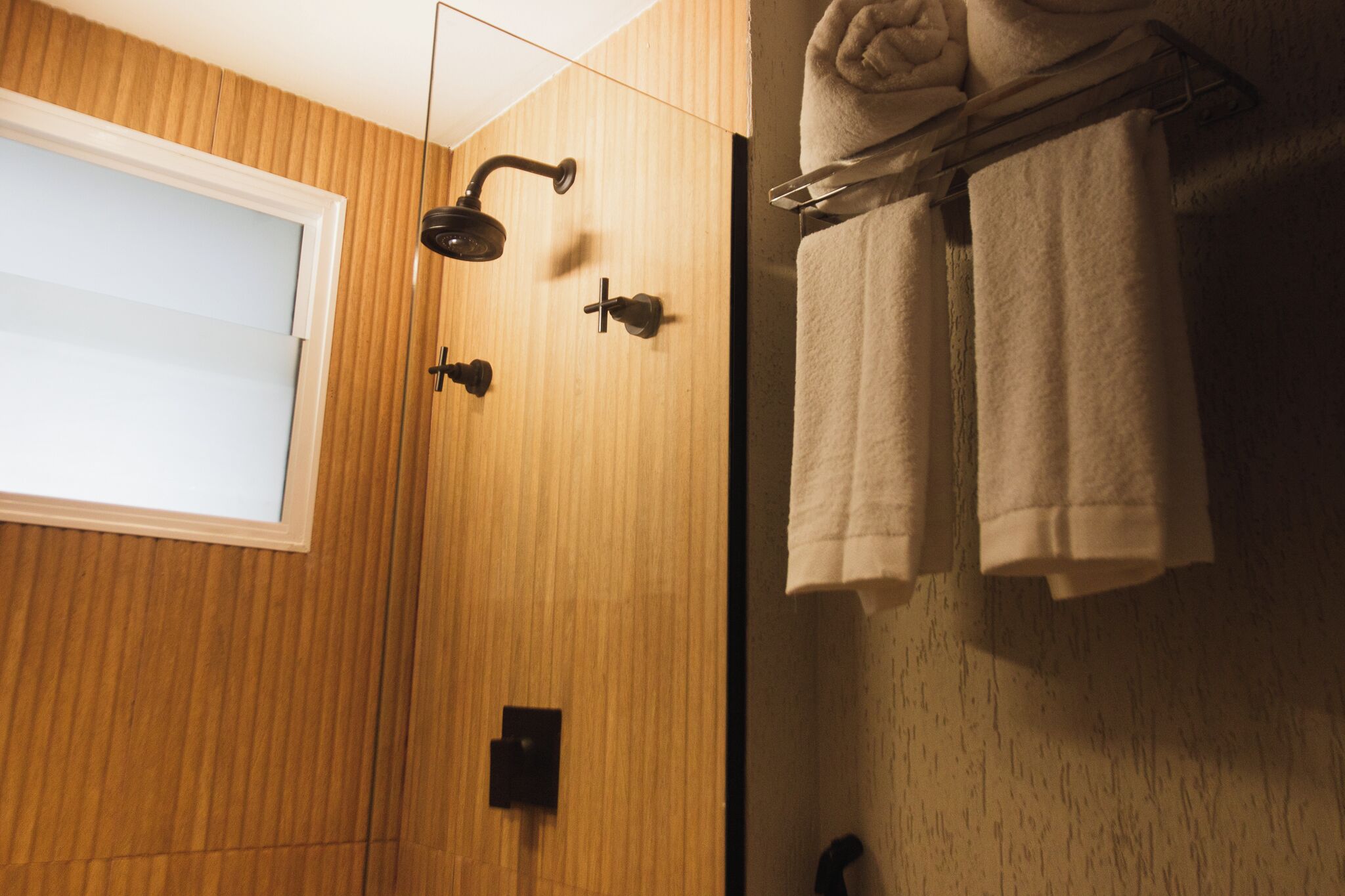 A wooden-paneled bathroom with a shower, a towel rack, and a window.
