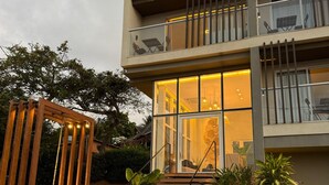 Un edificio moderno de dos pisos con base de piedra, un letrero que dice "VILLAGE PREMIERE" y un porche de madera con luces.