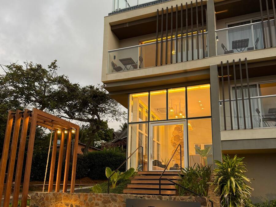 A modern two-story building with a stone base, a sign reading "VILLAGE PREMIERE," and a wooden pergola with lights.