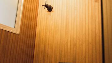 Ducha con pared de paneles de madera, un pequeño panel de control negro y una ventana con marco blanco.