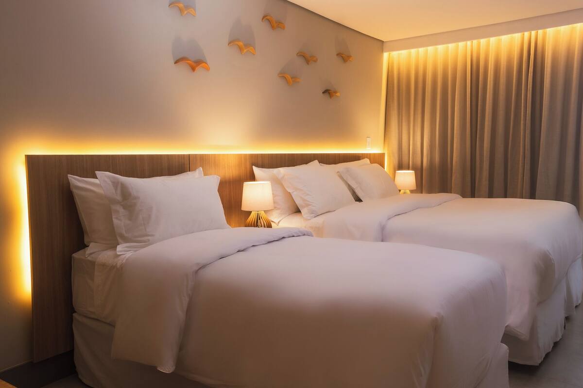 A hotel room with two beds, a wooden headboard, wall-mounted bird decorations, and a large window with curtains.