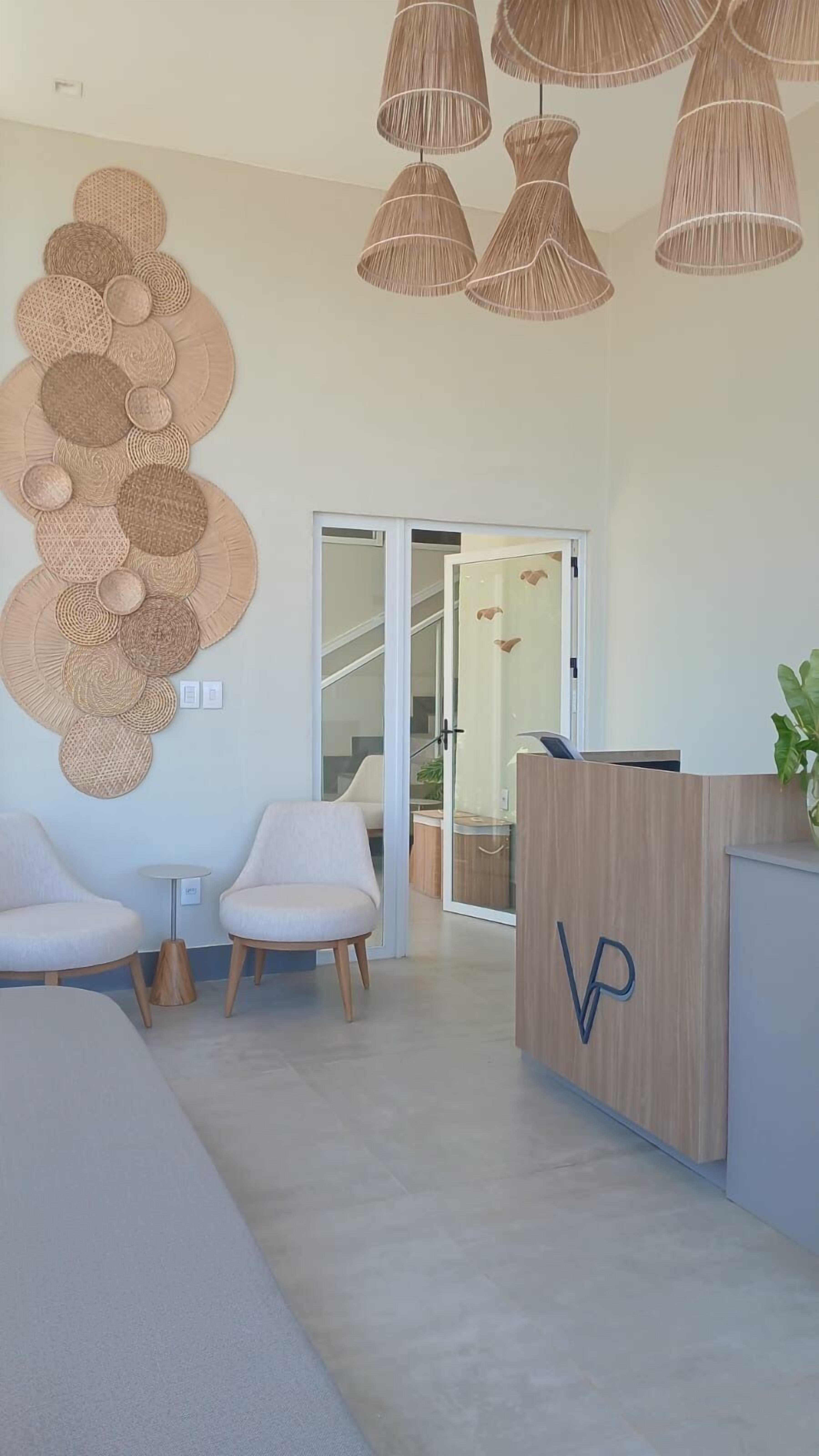 Un área de recepción moderna con un mostrador de madera, dos sillas blancas y una obra de arte tejida en la pared.