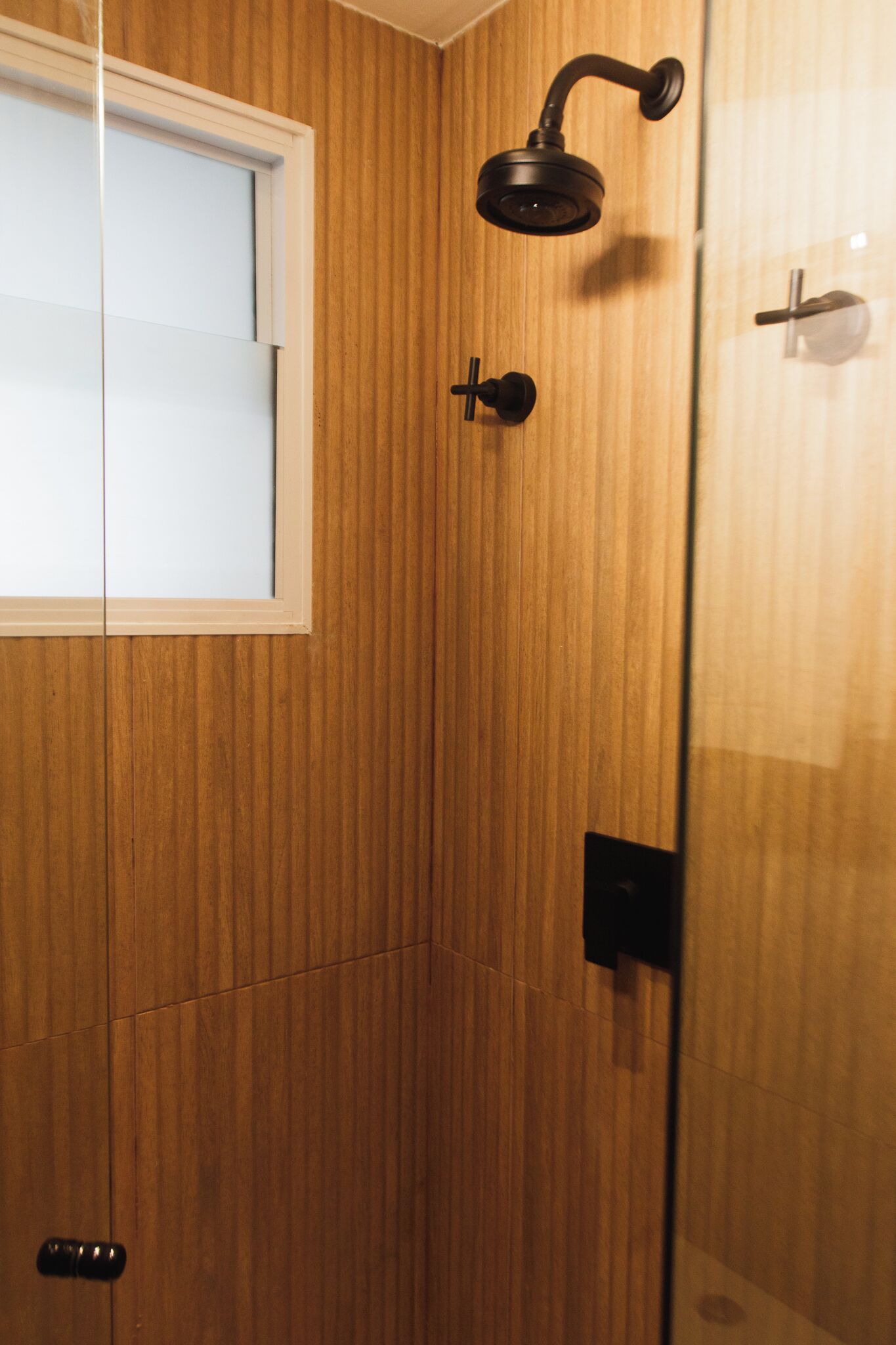 A wooden-paneled bathroom with a showerhead, a window, and a door.