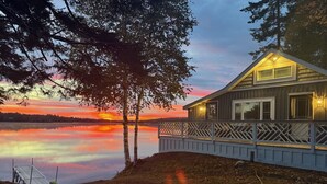 Una cabaña con terraza que da a un lago tranquilo al atardecer.