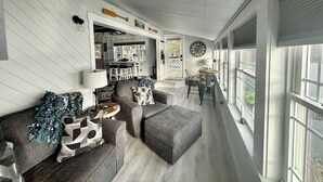 Amplia sala de estar con un conjunto de sofás, una mesa de centro y una mesa de comedor con sillas. Hay un ventanal que proporciona luz natural y vistas al exterior.