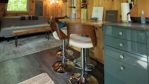 L’intérieur d’un chalet en bois comprend un canapé, une table à manger, un tabouret de bar et un coin cuisine.