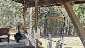 Un espace extérieur abrité doté d’une terrasse en bois, d’un barbecue, d’un hamac et offrant une vue sur les arbres.