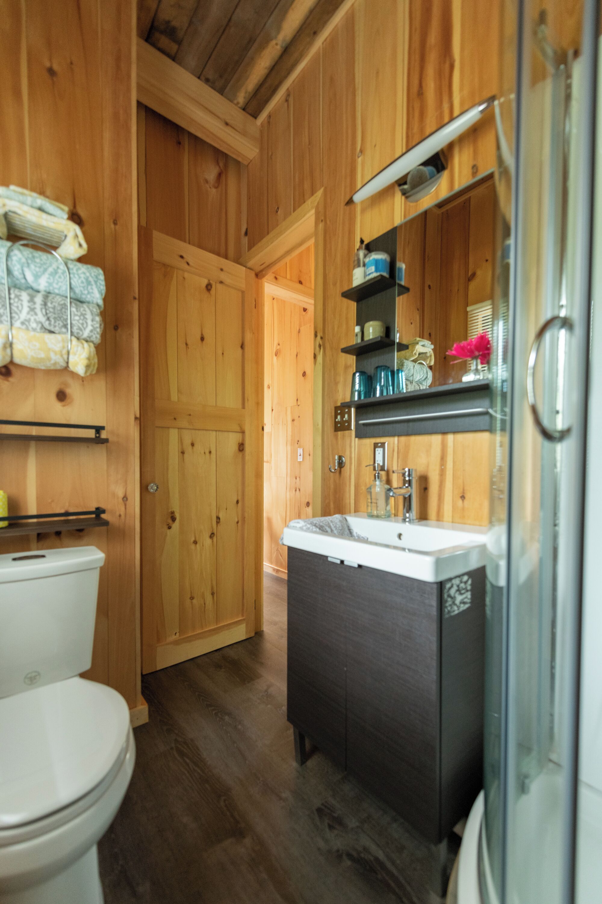 Une salle de bain aux murs lambrissés, équipée de toilettes, d’un lavabo et d’une douche.