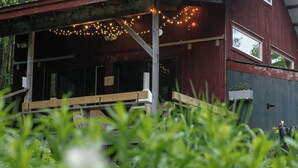 Un bâtiment de style rustique doté d’une terrasse en bois, de guirlandes lumineuses et d’une fenêtre donnant sur un jardin.