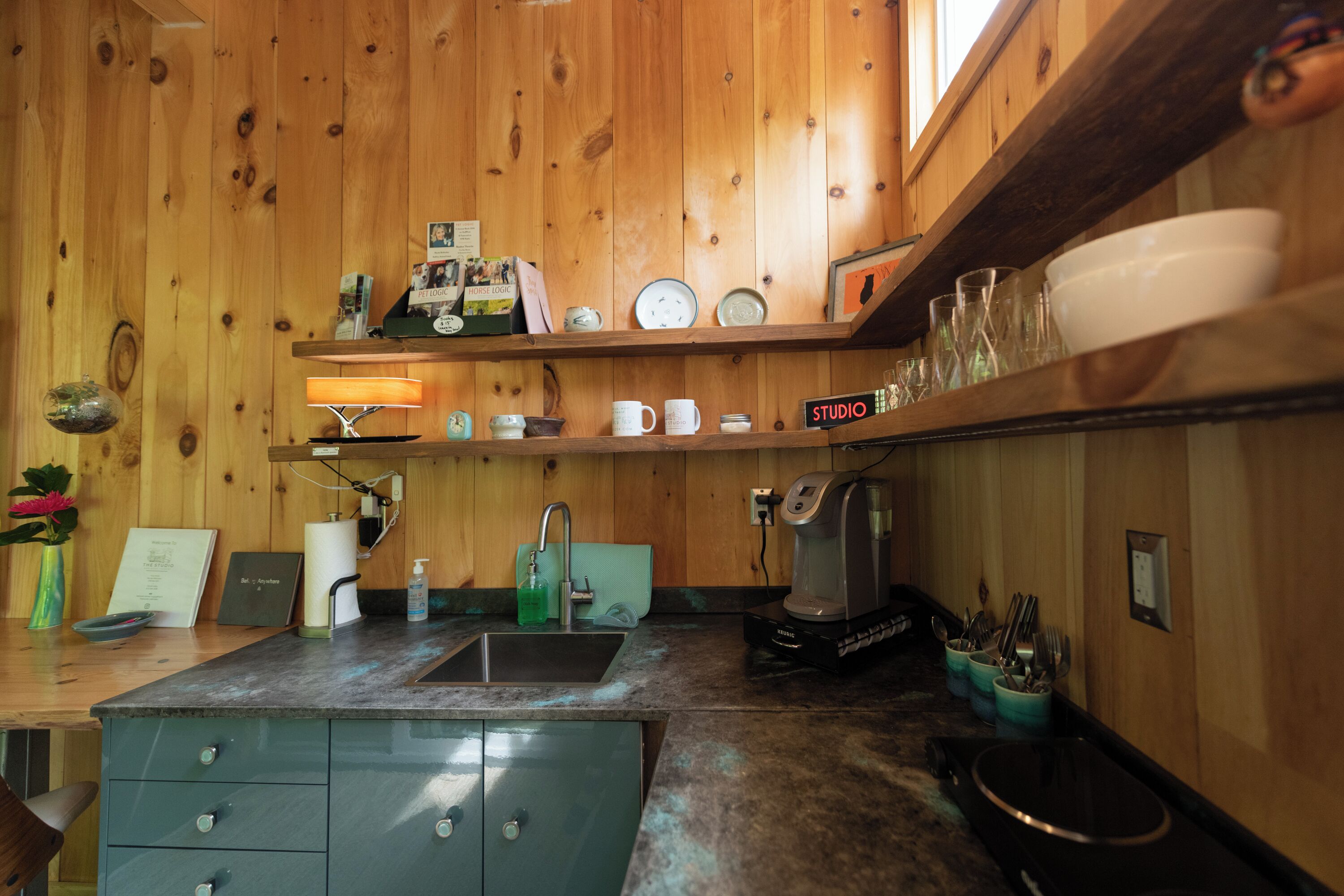A kitchen with wooden walls, a sink, a coffee maker, and various kitchen items on shelves.