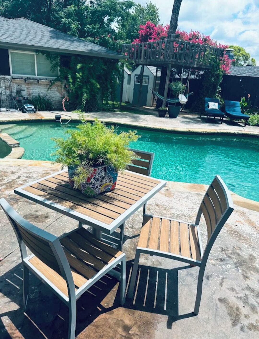 Ein Poolbereich mit Tisch und Stühlen, einem Blumentopf und einer Holzterrasse.