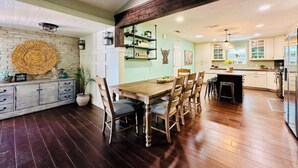 A spacious kitchen with wooden flooring, a dining area with a wooden table and chairs, and a kitchen island with a built-in sink.