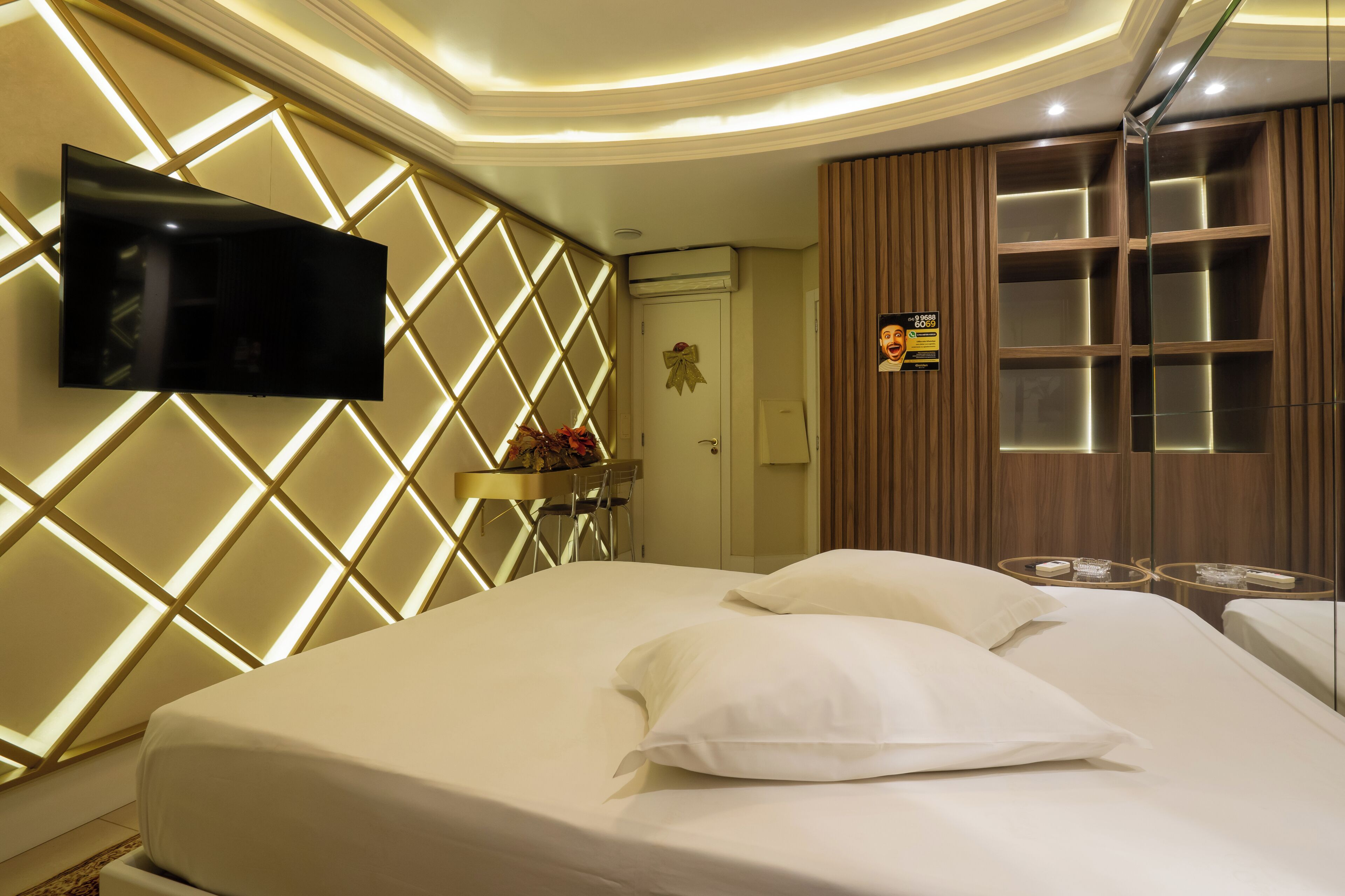 A hotel room with a bed, a mounted TV, a mirror, and a wooden panel wall.