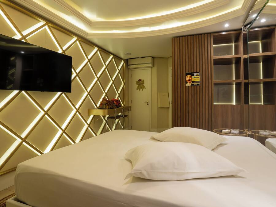 A hotel room with a bed, a mounted TV, a mirror, and a wooden panel wall.