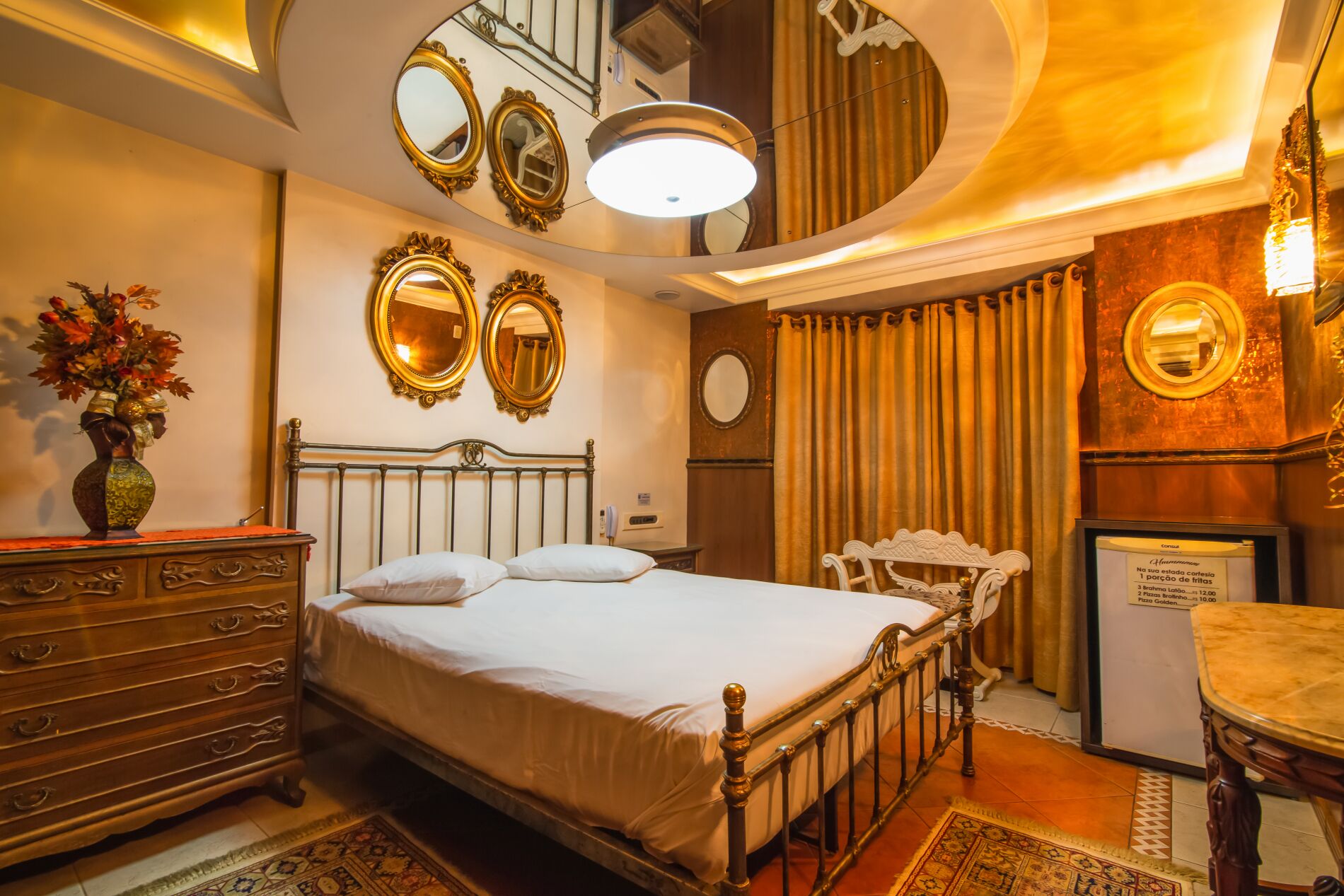 A hotel room with a bed, dresser, vanity with mirrors, a chair, and a small table.
