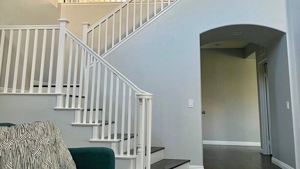 Un espacio habitable amplio con una escalera que sube a un nivel superior, un sofá verde y un cuadro en la pared.