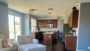 Amplia sala de estar con un ventanal grande, una zona de estar acogedora y una cocina con alacenas de madera y electrodomésticos modernos.