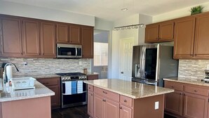 Una cocina moderna con gabinetes de madera, refrigerador de acero inoxidable, microondas, horno y encimeras de granito.
