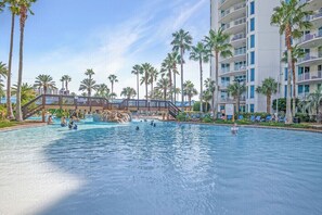 A swimming pool with palm trees, a waterfall feature, and a multi-story building with balconies. - The Palms Destin 2103 (Destin)