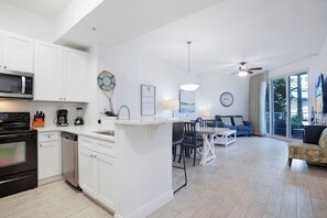 A modern kitchen with white cabinetry, a central island, and a dining area with a blue sofa and table. - The Palms Destin 2103 (Destin)