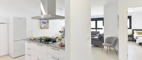 Eine moderne Küche mit weißen Schränken, einer Edelstahl-Dunstabzugshaube und einem Essbereich mit grauem Sofa und grauem Sessel.
