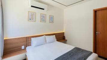 Una cama bien hecha con sábanas blancas, un plaid gris y un cabecero de madera. Encima de la cama, hay tres cuadros enmarcados en la pared.