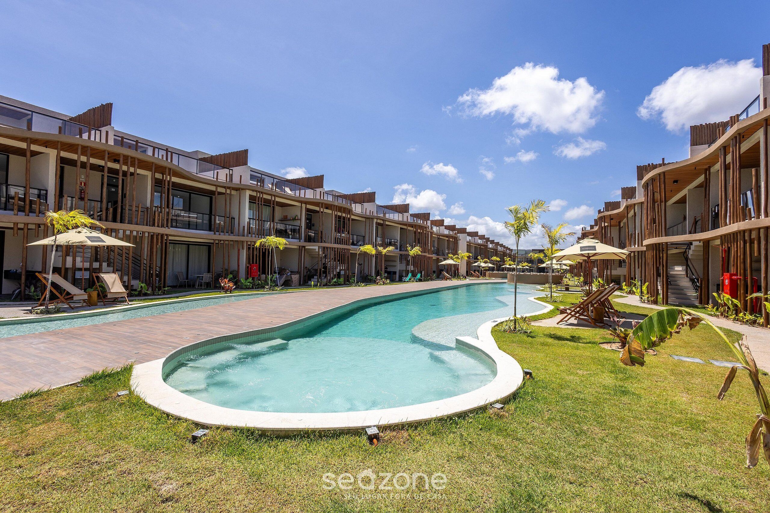 A modern hotel with a swimming pool, outdoor seating, and a clear blue sky.