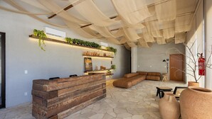 A modern interior with a stone floor, a wooden reception desk, a leather sofa, and a ceiling with fabric panels. - Apartments in Condo With Pool in Front of the Beach - NVB (Porto de Pedras)