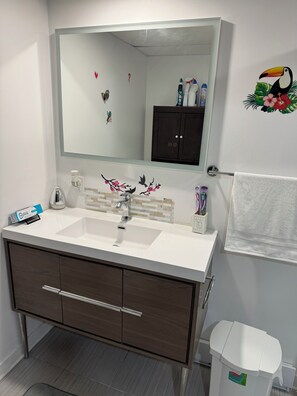 Un baño con lavamanos blanco, tocador de madera oscura, un espejo grande y un inodoro.