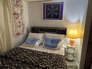 Una cama bien hecha con una manta de estampado de leopardo, dos almohadas, una mesita de noche con una lámpara y un cuadro en la pared.