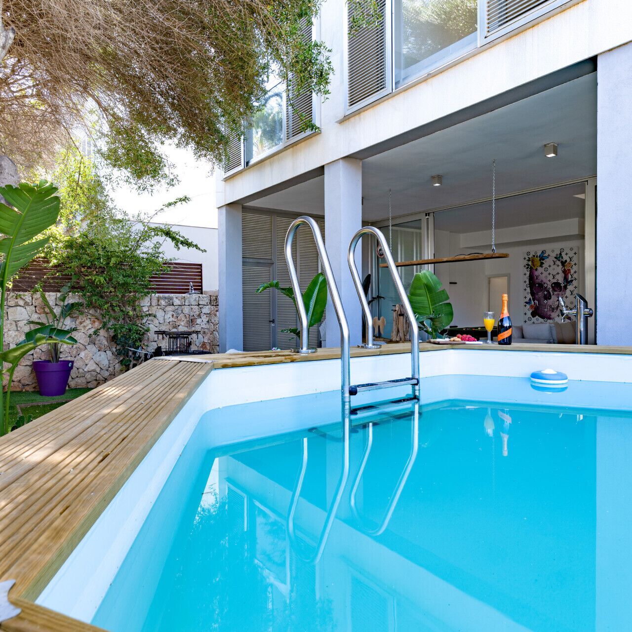 A swimming pool with metal ladders, a wooden deck, and a stone wall.