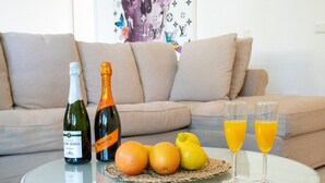 Ein Glastisch mit zwei Weinflaschen, einem Teller mit Orangen und Zitronen sowie zwei Gläsern Orangensaft.