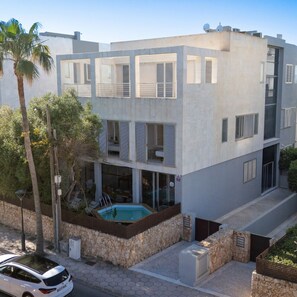 A modern multi-story building with a swimming pool, stone walls, and a car parked in front.