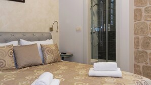 A hotel room with a bed, a bedside table, and a glass-enclosed shower area. - Queen Teuta Luxury Rooms Split (Split)