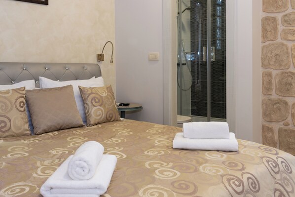 A hotel room with a bed, a bedside table, and a glass-enclosed shower area. - Queen Teuta Luxury Rooms Split (Split)