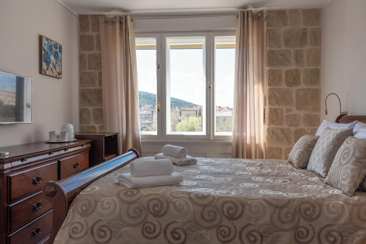 A hotel room with a bed, a dresser, a television, and a window with curtains.