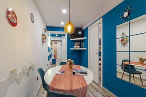 A dining area with a round table, chairs, a hanging pendant light, and a blue accent wall. - Mooniq Toledo Apartment   (Napoli)