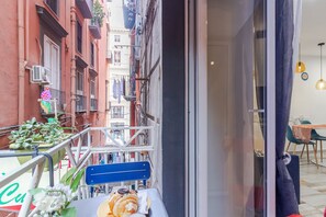 A narrow urban street with buildings on either side, a balcony with a table, chairs, and a plant. - Mooniq Toledo Apartment   (Napoli)