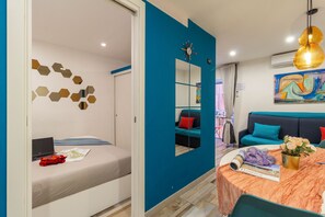 A modern room with a bed, a desk with a laptop, a dining table with a vase of flowers, and a large mirror. - Mooniq Toledo Apartment   (Napoli)