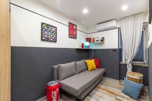 A room with a sofa, a red Coca-Cola can, a wall-mounted air conditioner, and a window with curtains. - Mooniq Toledo Apartment   (Napoli)
