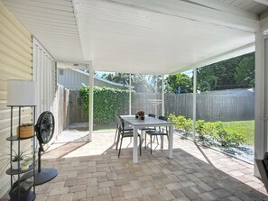 Een overdekt terras met een tafel, stoelen, een ventilator en een klein plankje met planten.