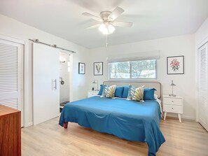 Een slaapkamer met een bed, nachtkastjes, een plafondventilator, een raam en een deur.