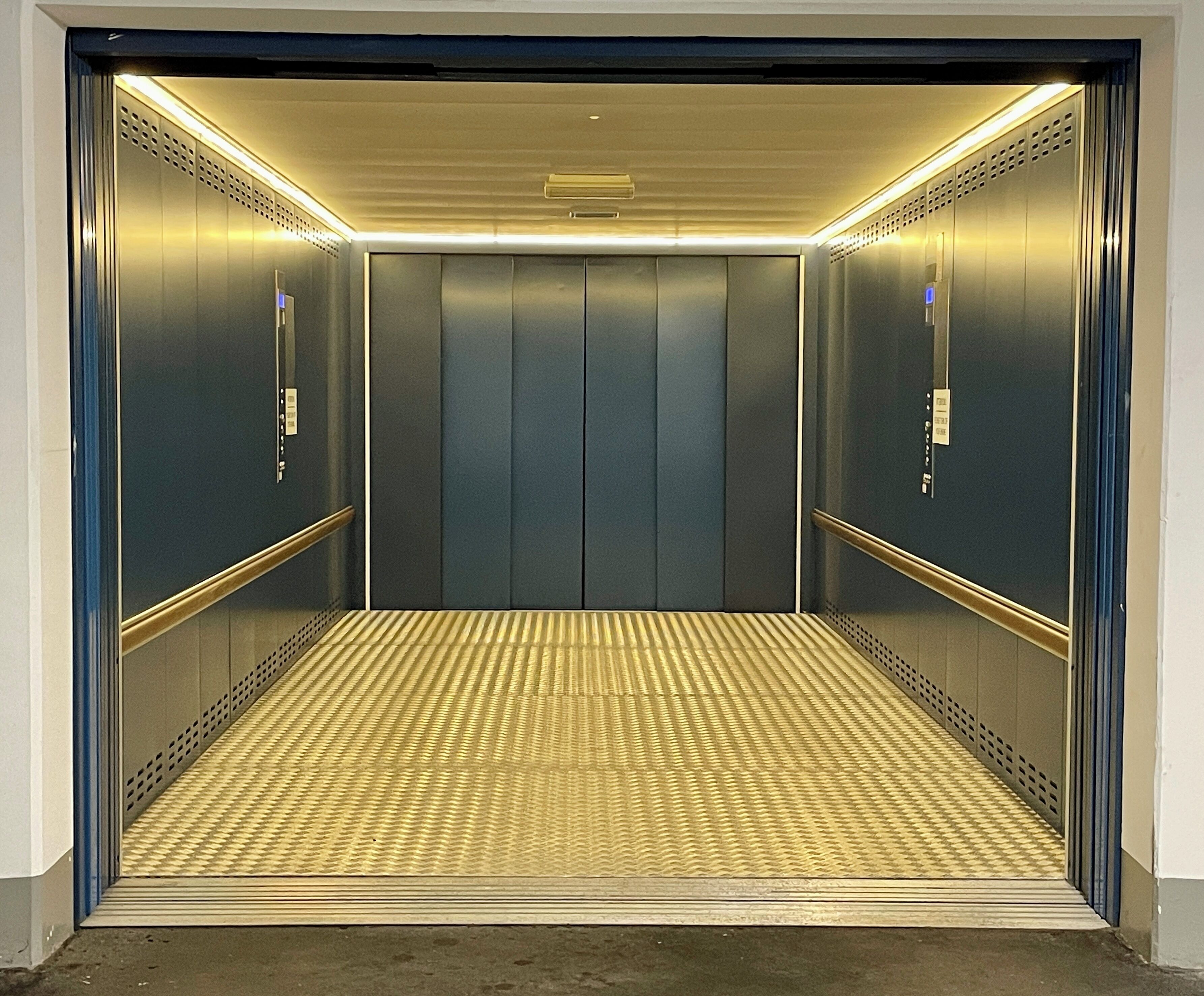 Ein Aufzug mit Metallwänden, einem strukturierten Boden und einer Decke mit Lüftungsöffnungen.
