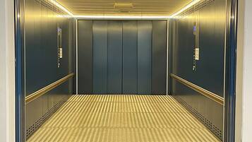 Ein Aufzug mit Metallwänden, einem strukturierten Boden und einer Decke mit Lüftungsöffnungen.